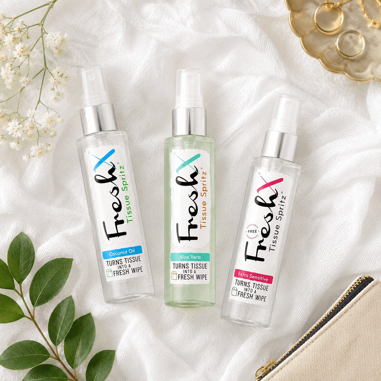 Three FreshX tissue spritz bottles on a white fabric background with flowers and jewellery.
