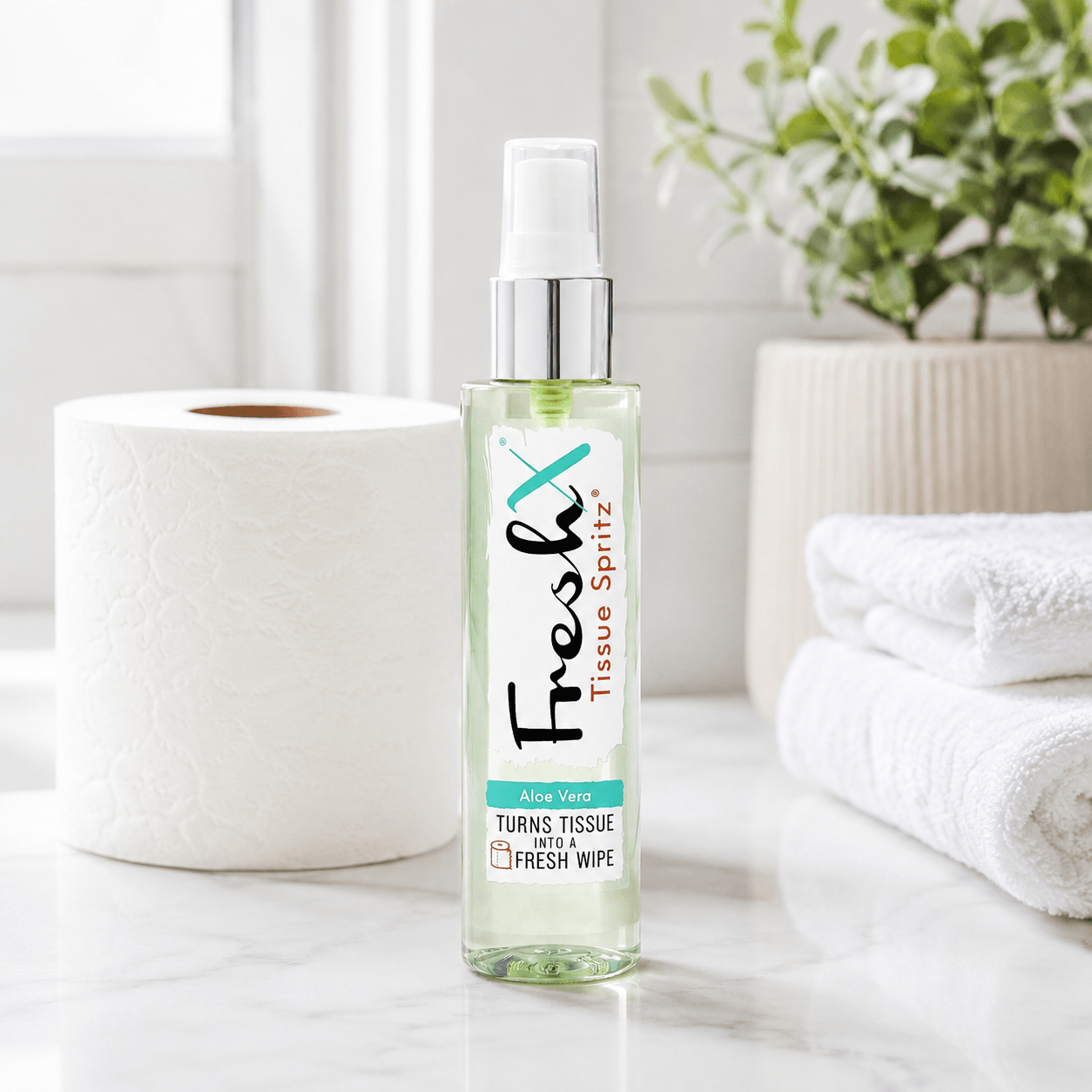 Bottle of FreshX Tissue Spritz on a bathroom counter with tissues and a plant in the background.