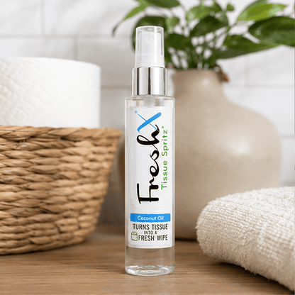 Clear spray bottle labeled 'FreshX Tissue Spritz' on a wooden surface with a plant and basket in the background.