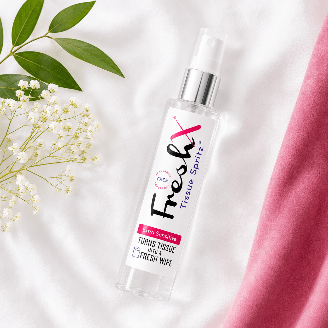 Bottle of FreshX Tissue Spritz on a white background with pink fabric and green leaves.