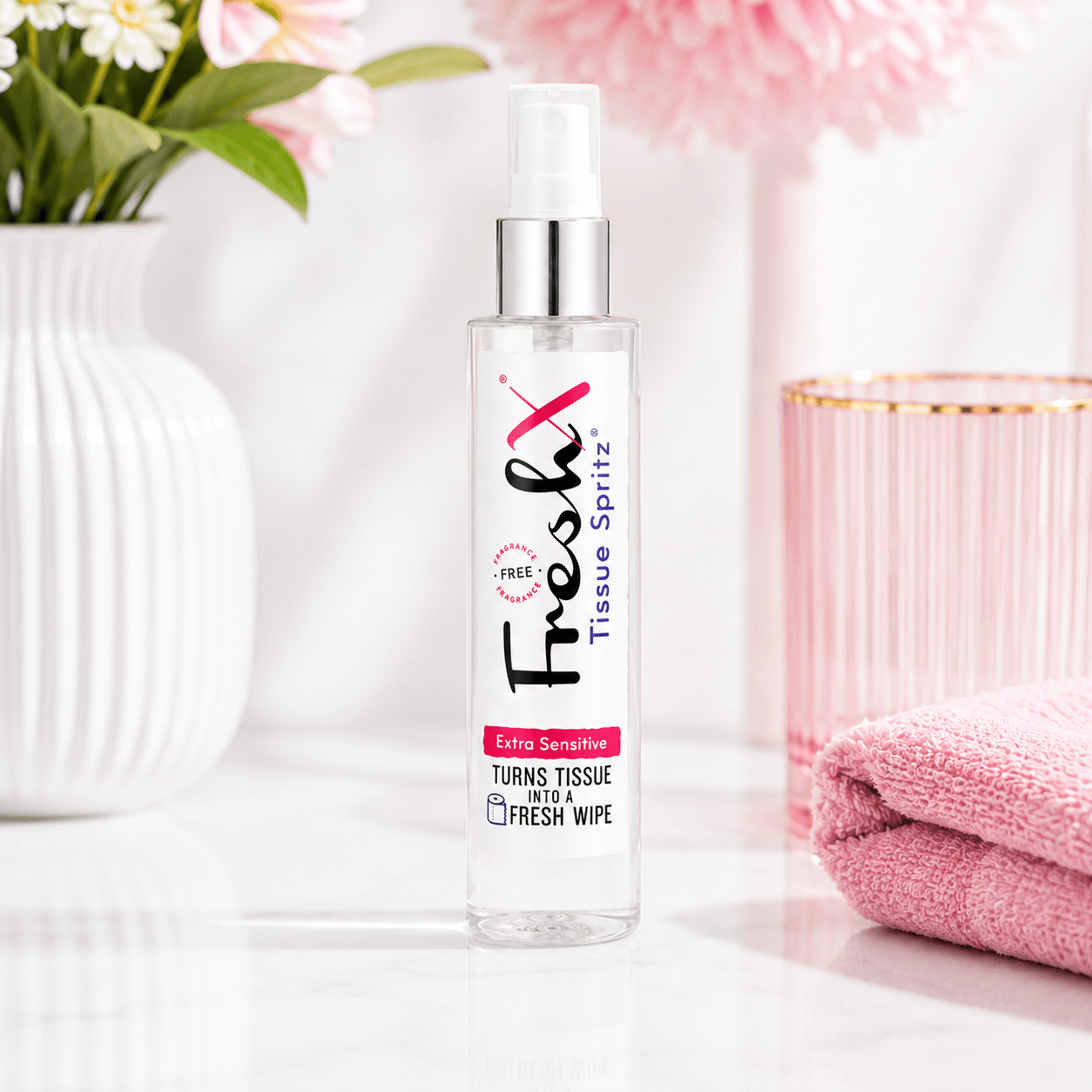FreshX Tissue Spritz bottle on a white surface with pink towel and flowers in the background
