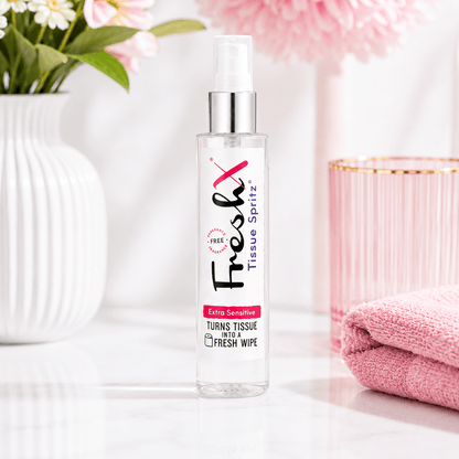 FreshX Tissue Spritz bottle on a white surface with pink towel and flowers in the background