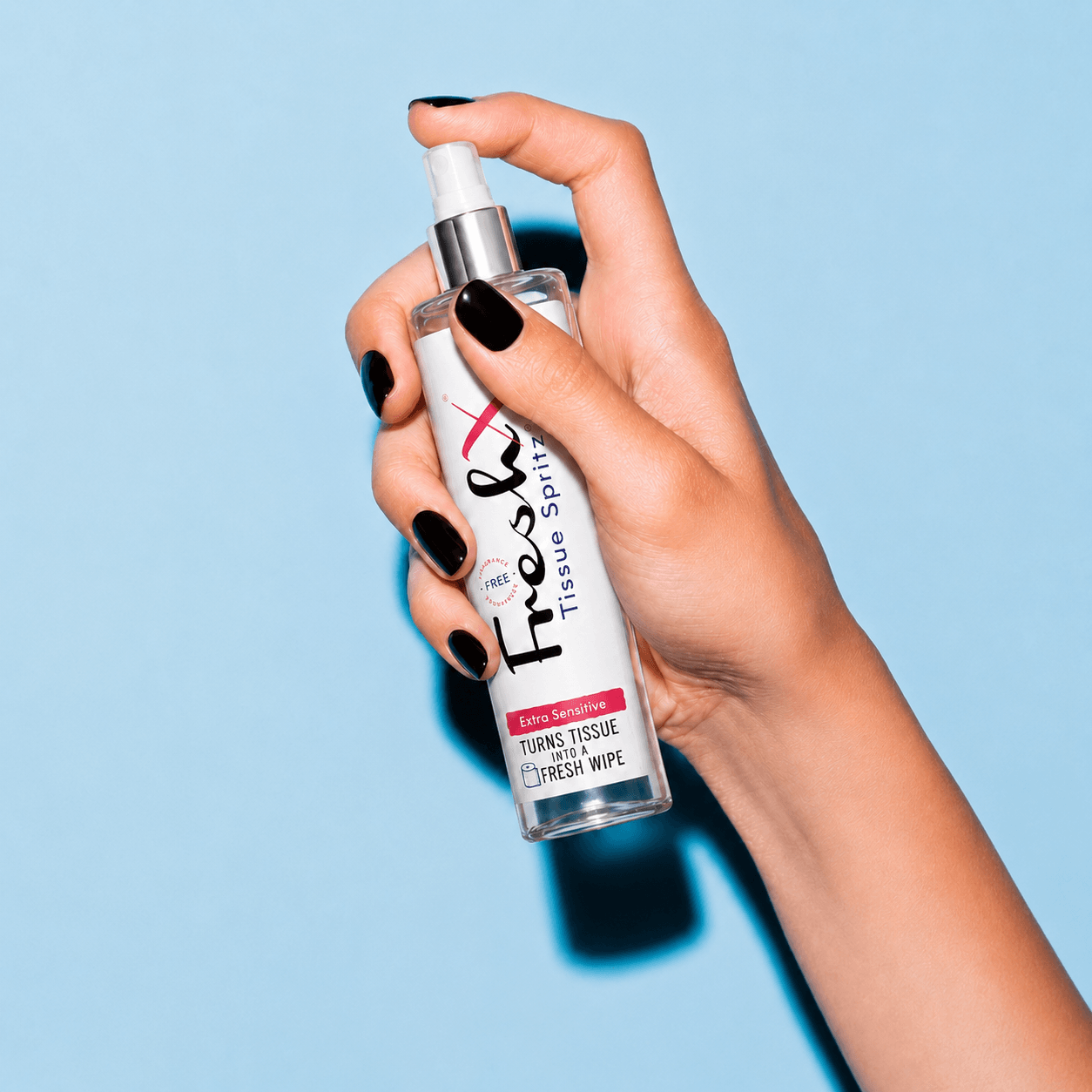 Hand holding a bottle of FreshX Tissue Spray against a light blue background